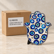 Hamsa Hand Evil Eye Decor with Stand — Box of 12 — 12 × Hamsa Hand Evil Eye Decor with Stand. Representative samples beside illustrative wholesale carton.