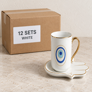 Evil Eye Mugs with Hamsa Trays — Box of 12 — 12 × White. Representative samples beside illustrative wholesale carton.